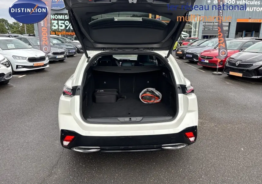 Vue arrière ouverte sur le coffre d'une Peugeot 308 SW hybride blanc nacré métal, avec un sac et une valise à l'intérieur.