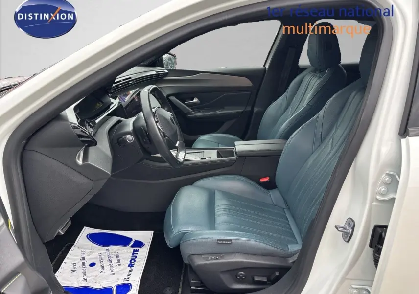 Intérieur côté conducteur de la Peugeot 308 SW hybride blanc nacré, sièges cuir bleu et tableau de bord moderne.