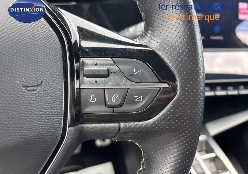 Gros plan sur les commandes au volant en cuir perforé noir du Peugeot 308 SW hybride, avec tableau de bord flou en arrière-plan.