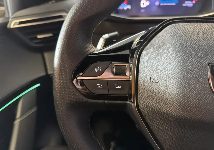 Gros plan sur la partie gauche du volant perforé noir du Peugeot 208 Hybrid 145 e-DCS6 GT avec commandes intégrées.