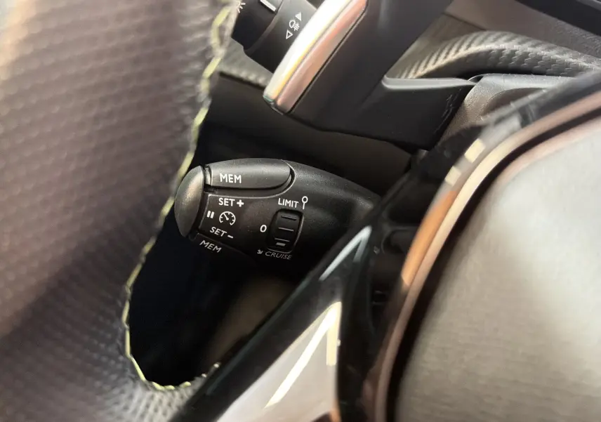 Gros plan sur la commande de régulateur de vitesse à gauche du volant d’une Peugeot 208 Hybrid 145 GT noir Perla.