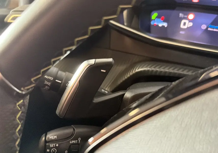 Gros plan intérieur sur la commande de régulateur de vitesse et palettes au volant, finition noire avec surpiqûres contrastées.
