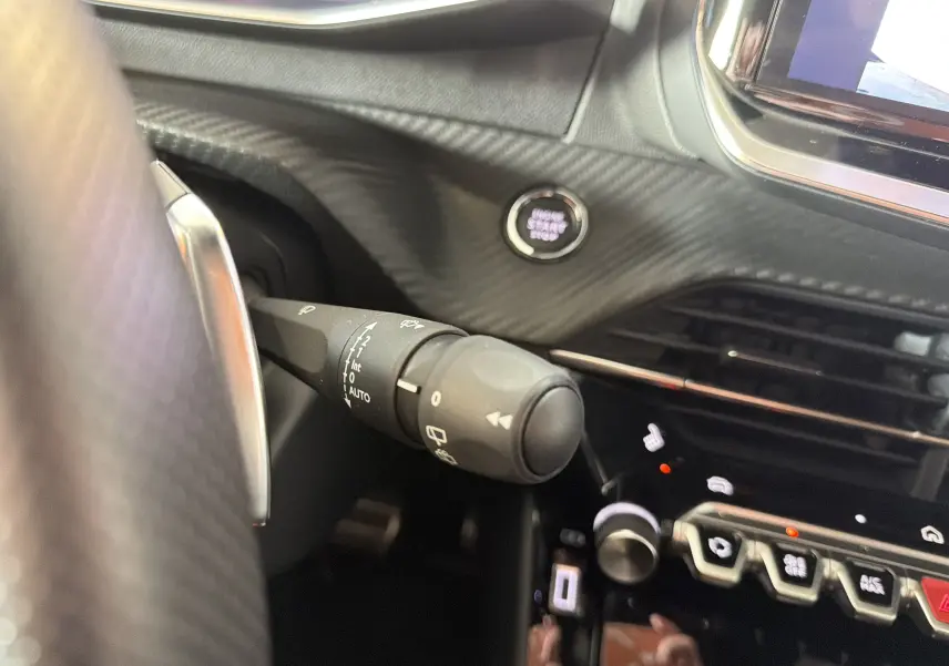 Détail intérieur du tableau de bord noir du Peugeot 208 Hybrid 145 GT, avec bouton start/stop et commandes au volant visibles.