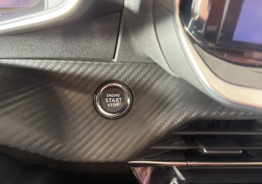 Détail intérieur du tableau de bord de la Peugeot 208 Hybrid 145 GT 2025, bouton Start/Stop sur finition carbone noir.