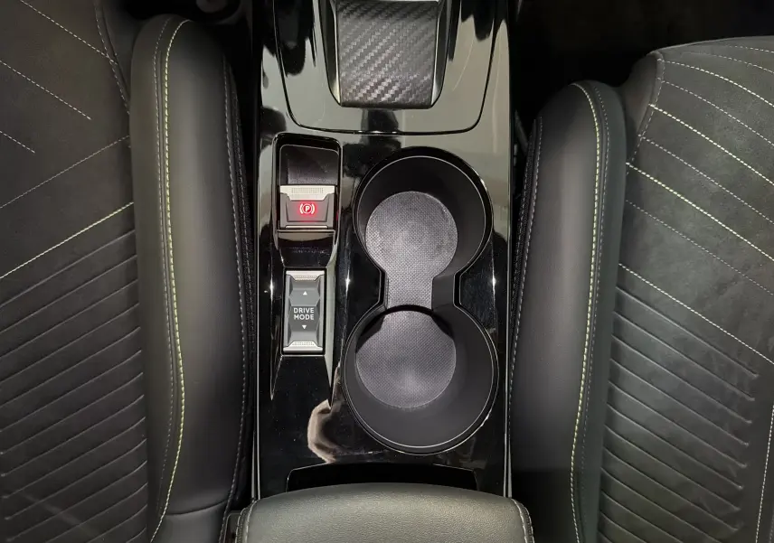 Vue plongeante sur la console centrale noire brillante de la Peugeot 208 Hybrid 145 GT avec surpiqûres vertes et porte-gobelets.