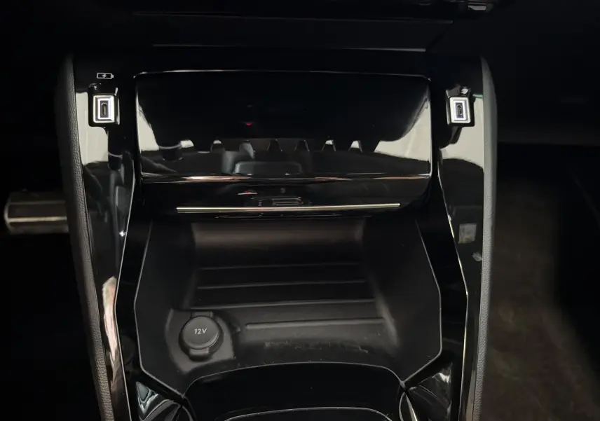 Gros plan sur la console centrale noire brillante de la Peugeot 208 Hybrid 145 e-DCS6 GT avec prise 12V et ports USB.