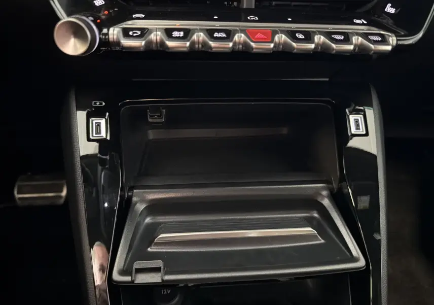 Vue rapprochée de la console centrale noire brillante du Peugeot 208 Hybrid 145 GT, avec commandes tactiles et rangement ouvert.
