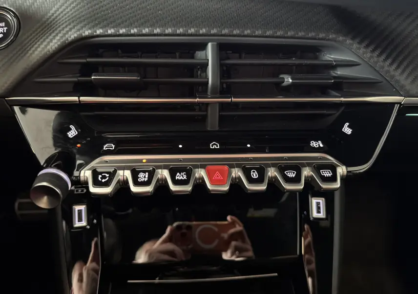 Vue rapprochée du tableau de bord noir de la Peugeot 208 HYBRID 145 GT, avec commandes tactiles et surpiqûres vertes visibles.