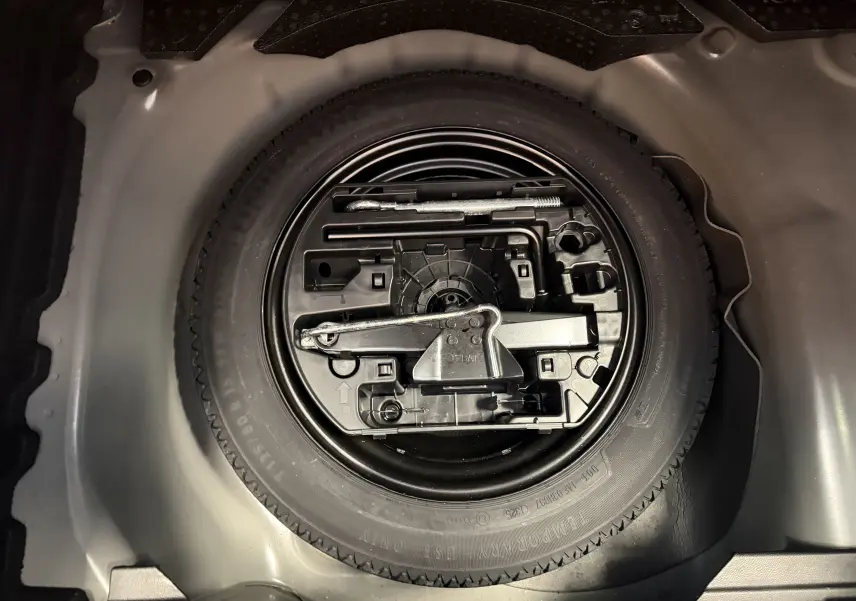 Vue en plongée sur la roue de secours et les outils de bord rangés dans le coffre d'une Peugeot 208 noir perla.