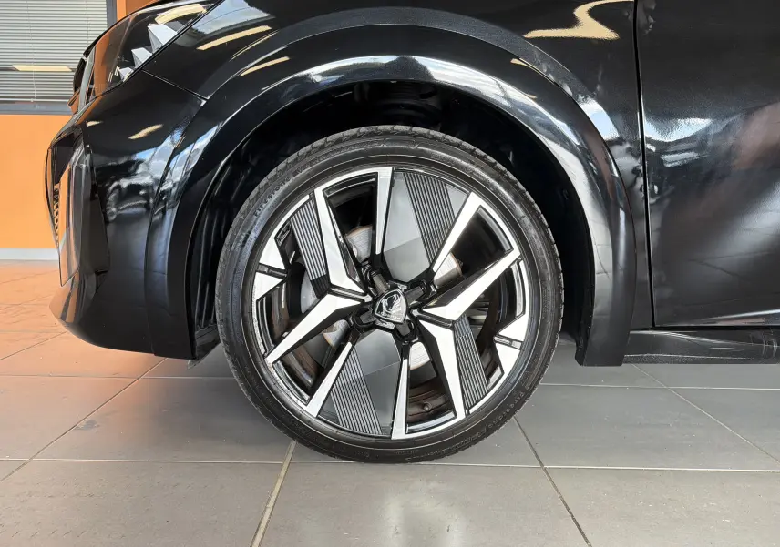Gros plan sur la roue avant gauche du Peugeot 208 Hybrid 145 GT noir Perla avec jante alliage 17 pouces bicolore.