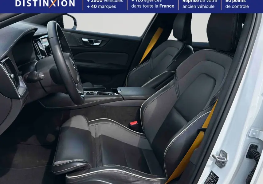 Intérieur avant droit d'une Volvo S60 blanche 2021 avec sièges sport cuir/tissu anthracite et ceintures jaunes.