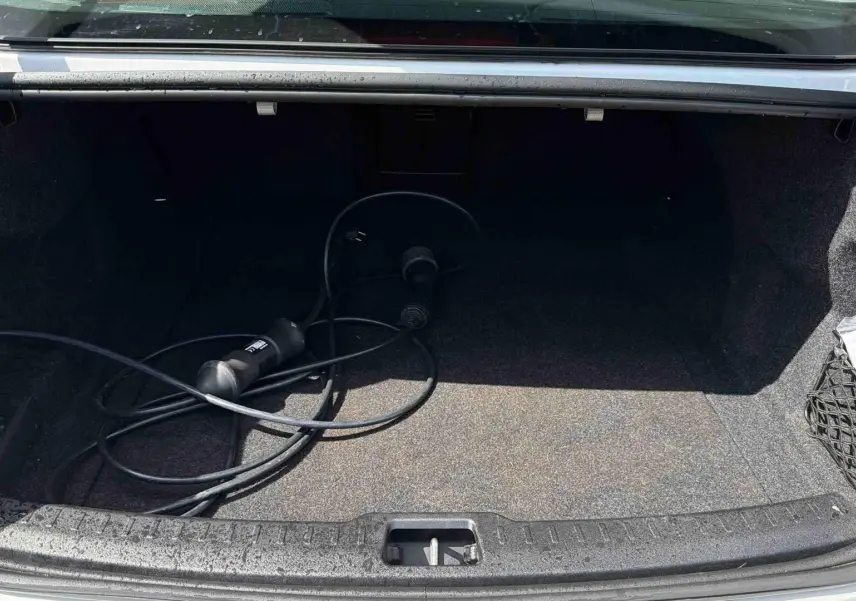 Coffre ouvert d'une Volvo S60 blanche de 2021 avec câble de recharge électrique visible à l'intérieur.