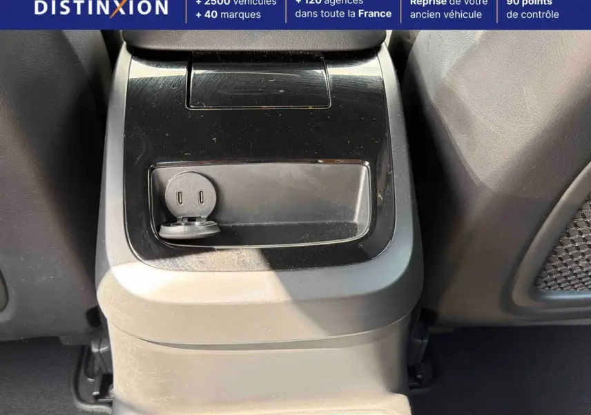 Prise USB et console centrale en plastique noir mat dans l'habitacle arrière d'une Volvo S60 blanche.