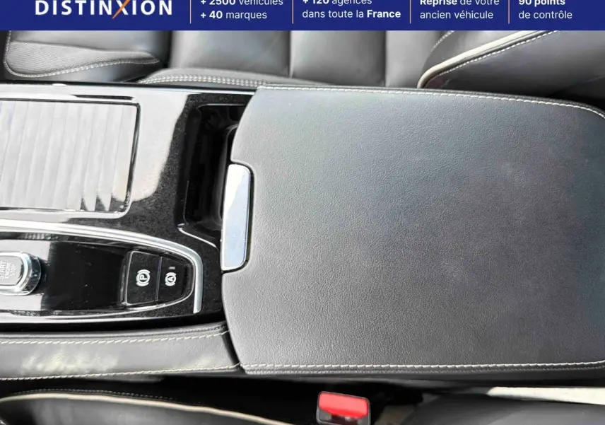 Gros plan sur la console centrale en cuir noir avec surpiqûres beige et commandes électroniques d'une Volvo S60 blanche.