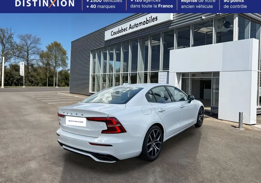Vue 3/4 arrière droite d'une Volvo S60 T8 blanche avec jantes noires et calandre brillante, devant un showroom.