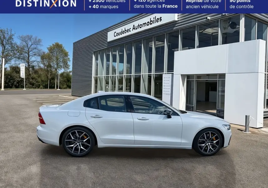 Profil droit d'une Volvo S60 T8 Twin Engine blanche avec jantes 19 pouces style Y noir et freins dorés, devant un bâtiment.