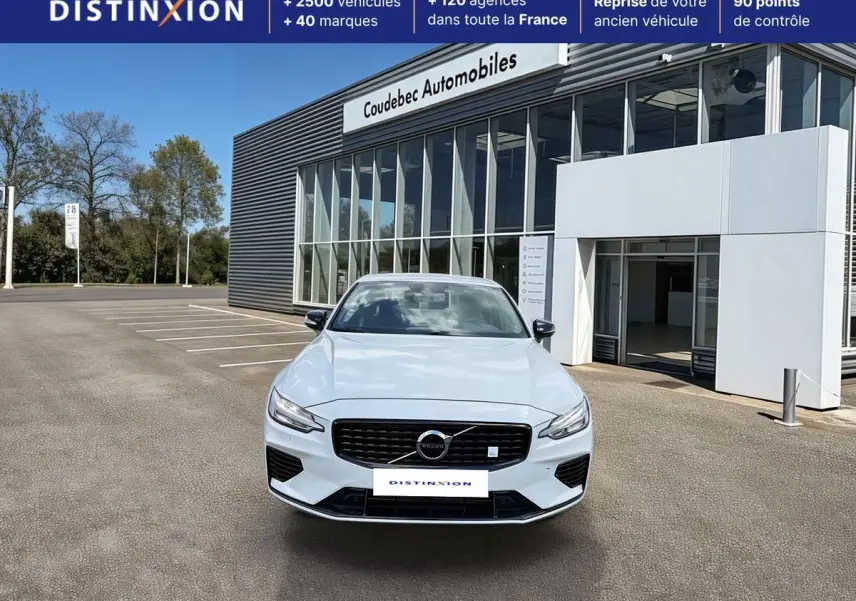 Vue avant d'une Volvo S60 blanche avec calandre noire brillante et feux LED, stationnée devant un bâtiment commercial.