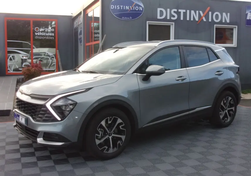 KIA SPORTAGE gris perle en 3/4 avant droit, avec calandre distinctive et jantes alliage stylisées.