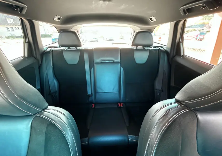 Vue intérieure arrière du Volvo XC60 gris 2016, montrant les sièges arrière en cuir noir avec appuie-têtes et ceinture de sécurité.