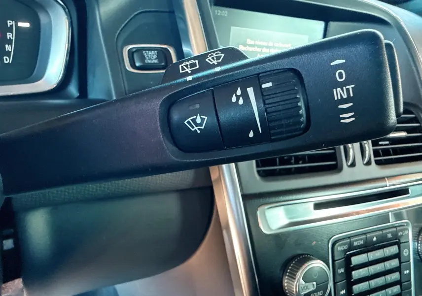 Gros plan sur la commande d’essuie-glace du Volvo XC60 gris, avec tableau de bord et bouton start/stop en arrière-plan.