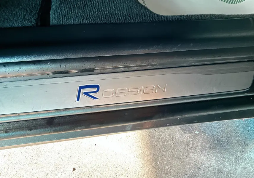 Gros plan sur la plaque de seuil de porte R-Design d'un Volvo XC60 gris, mettant en valeur la finition sportive.