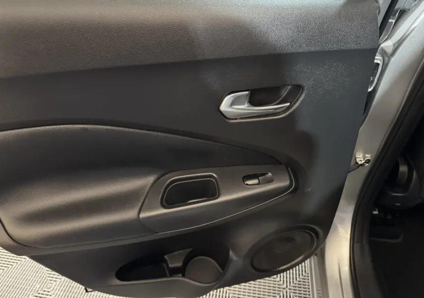 Vue rapprochée de la porte intérieure côté droit du Nissan Juke gris clair, avec poignée argentée et haut-parleur intégré.