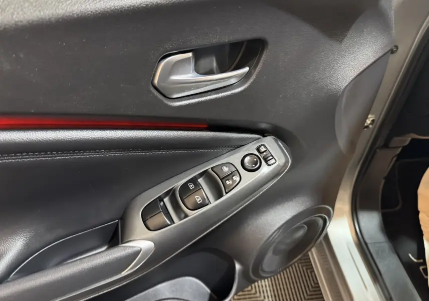 Vue rapprochée de la porte avant gauche gris clair du Nissan Juke 2025 avec commandes de vitres et poignée alu.