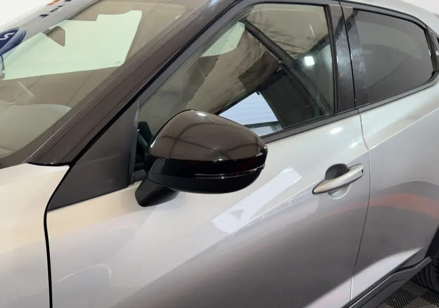 Vue rapprochée du côté gauche d’un Nissan Juke gris clair avec rétroviseur noir brillant et poignée de porte visible.