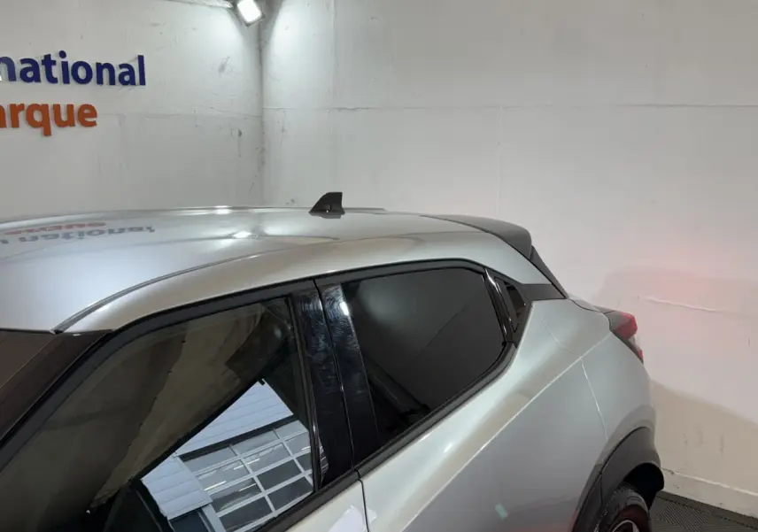 Vue latérale arrière droite du Nissan Juke gris clair avec vitres teintées et toit compact en intérieur showroom.
