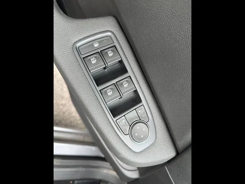 Gros plan sur les commandes des vitres électriques et réglages des rétroviseurs côté conducteur d'une Renault Clio gris 2025.