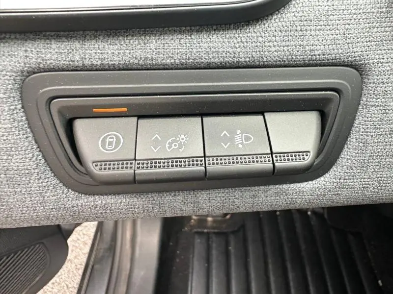 Gros plan sur les commandes de réglage des feux et verrouillage intérieur du tableau de bord d'une Renault Clio gris 2025.