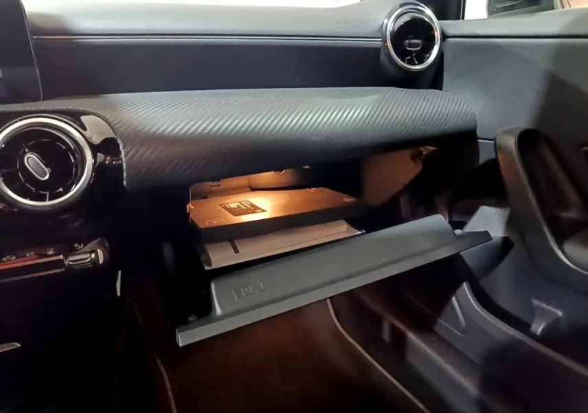 Vue intérieure de la boîte à gants ouverte côté passager dans une Mercedes Classe A noire avec tableau de bord texturé.