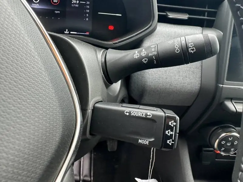 Gros plan sur les commandes au volant noir et gris de la Renault Clio 2025, avec tableau de bord partiellement visible.