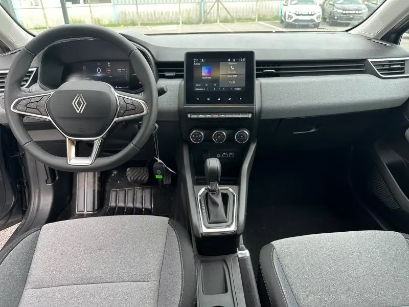Vue intérieure avant de la Renault Clio 2025 avec tableau de bord gris, volant multifonction et écran tactile central.