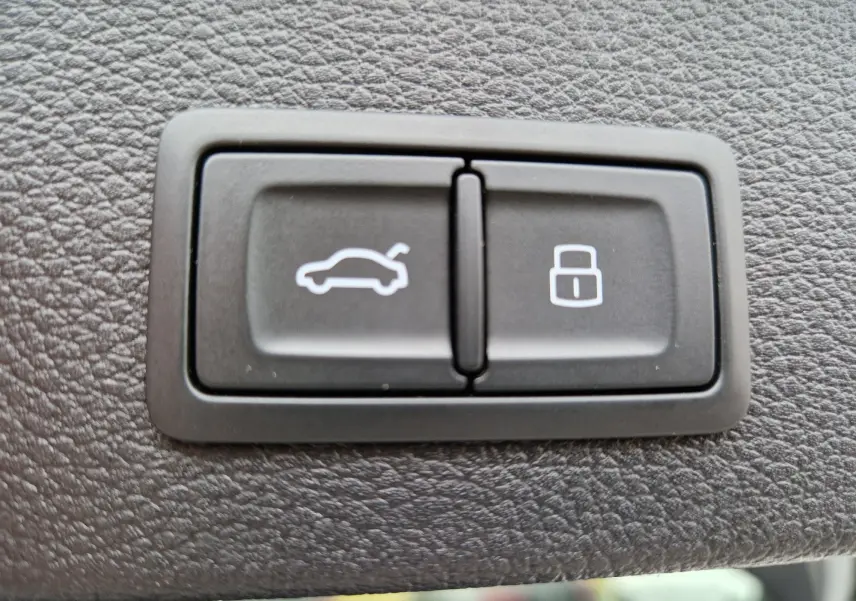 Gros plan sur les boutons d'ouverture électrique du capot arrière et de verrouillage, sur tableau de bord noir texturé.