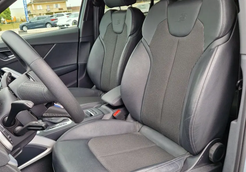 Vue intérieure côté conducteur de l'Audi Q2 35 TFSI 2023 gris flèche, sièges sport S line en cuir noir avec logo S embossé.
