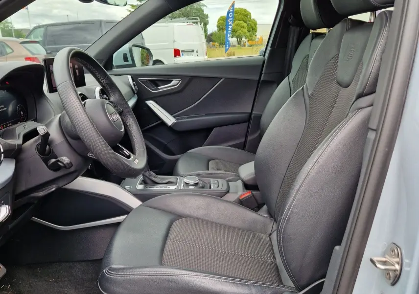 Vue intérieure côté conducteur de l'Audi Q2 35 TFSI 2023 gris flèche, sièges S line en cuir noir avec détails aluminium brossé.
