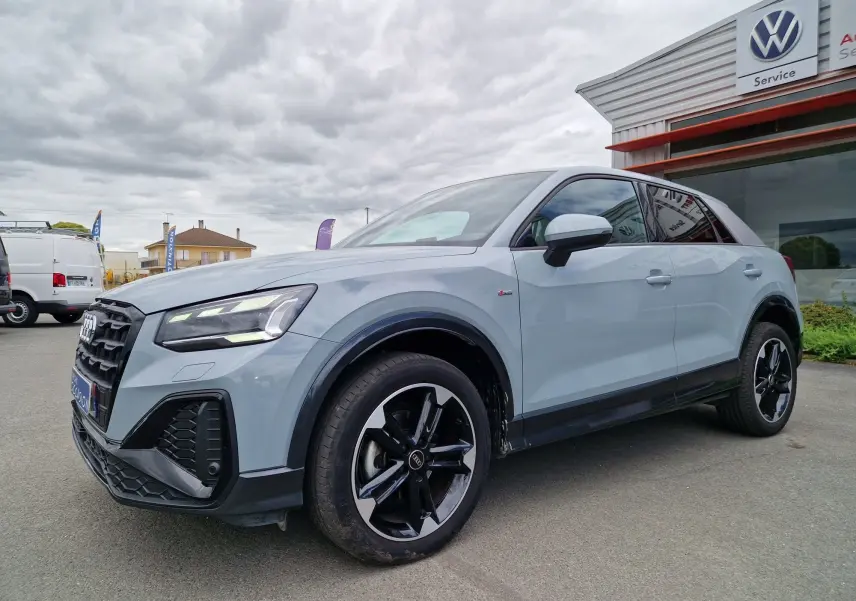 Audi Q2 35 TFSI 2023 gris flèche en 3/4 avant droit, avec jantes sport noires et finition S line visible.