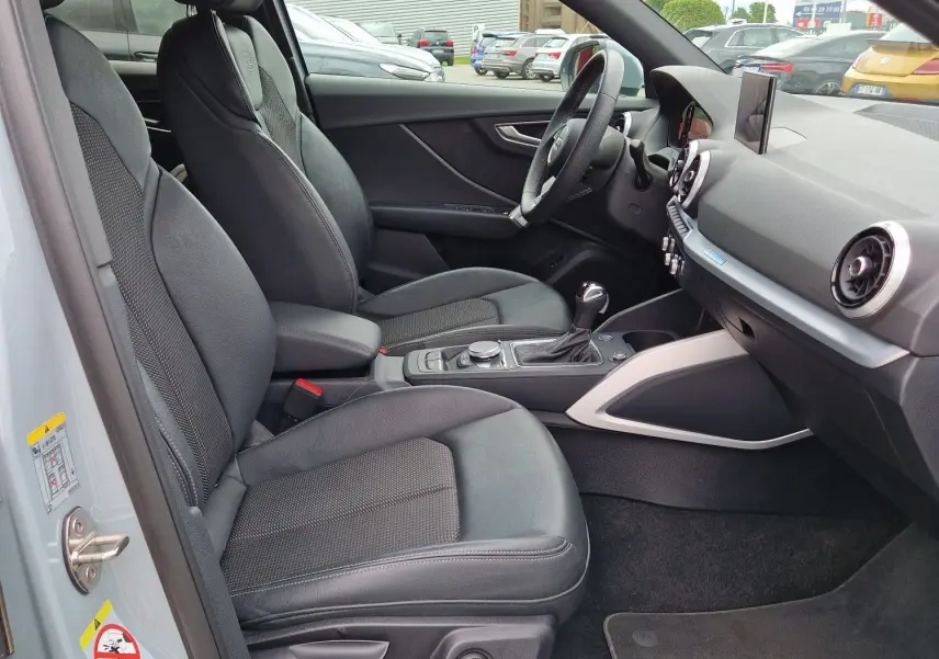 Vue intérieure côté conducteur de l'Audi Q2 2023 gris flèche, avec sièges sport S line en cuir et tableau de bord moderne.