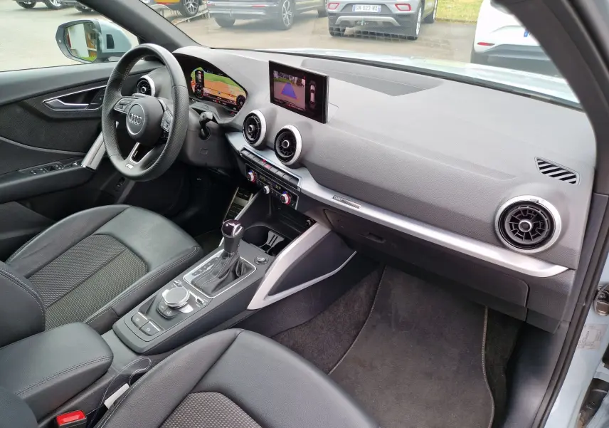Vue intérieure côté conducteur de l'Audi Q2 35 TFSI 2023, avec tableau de bord gris, écran MMI et volant multifonction.