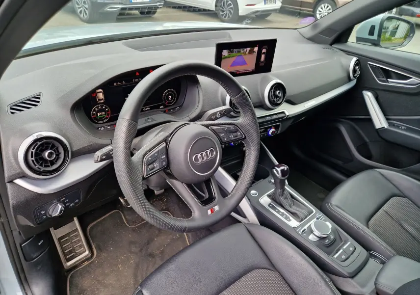 Vue intérieure côté conducteur de l'Audi Q2 35 TFSI 2023, avec volant S line, écran MMI et sellerie noire.
