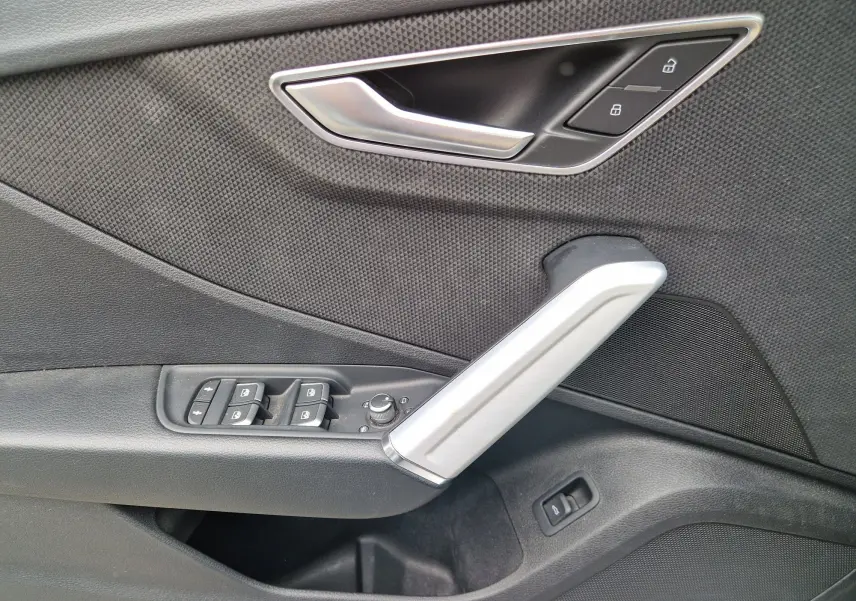 Détail de la porte avant gauche de l’Audi Q2 35 TFSI 2023 avec poignée aluminium brossé et commandes de vitres.