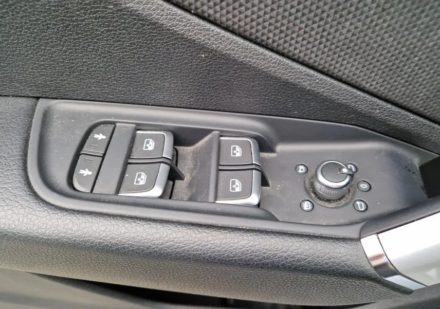Gros plan sur les commandes de lève-vitres et réglage des rétroviseurs côté conducteur de l’Audi Q2 gris flèche.