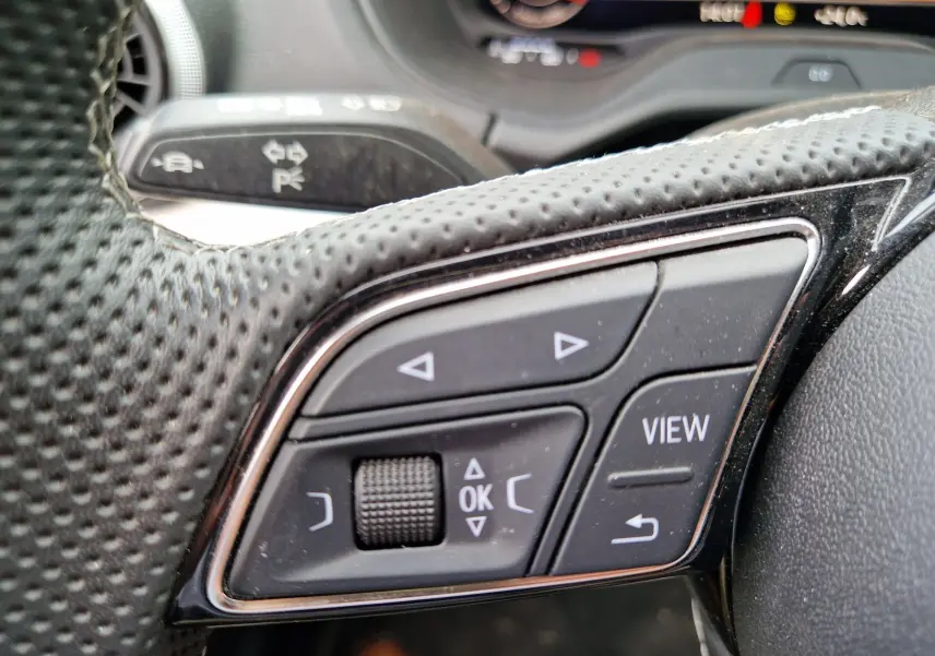 Gros plan sur les commandes multifonctions au volant perforé de l’Audi Q2 35 TFSI S line 2023, avec affichage digital en arrière-plan.