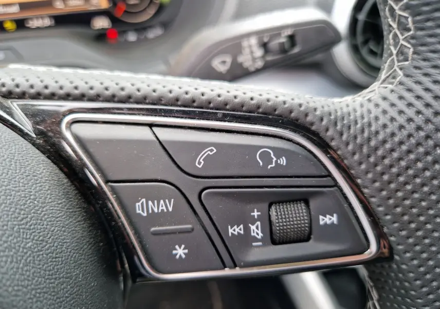 Gros plan sur les commandes multifonctions au volant perforé de l’Audi Q2 35 TFSI gris flèche, finition S line.