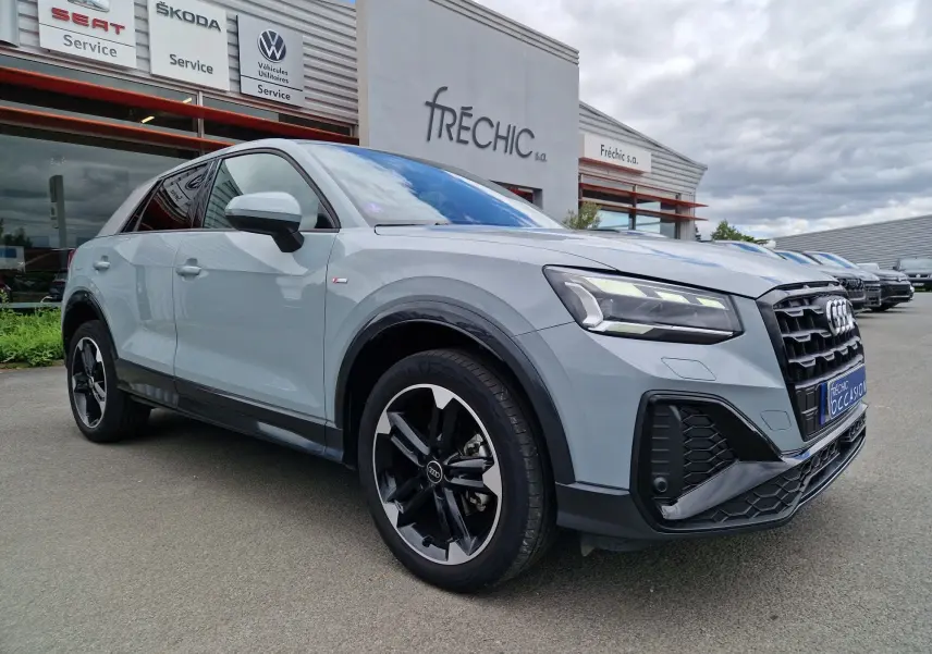 Audi Q2 35 TFSI 2023 gris flèche vue 3/4 avant droit, finition S line avec jantes sport 18 pouces noires.