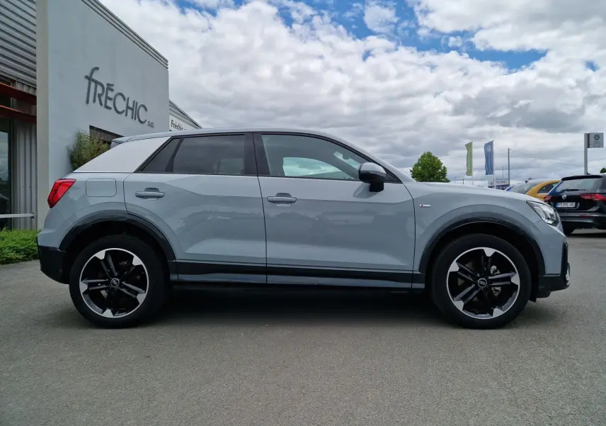 Audi Q2 35 TFSI 2023 gris flèche vue de profil côté gauche, avec jantes sport 18 pouces et toit contrasté blanc.