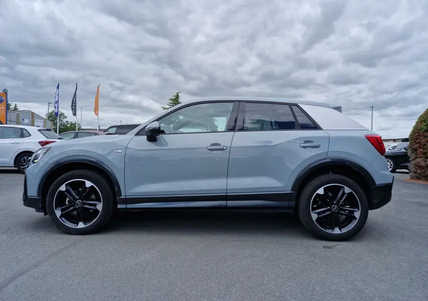 Audi Q2 35 TFSI S line gris flèche vue de profil côté gauche avec jantes sport noires 18 pouces et toit clair.
