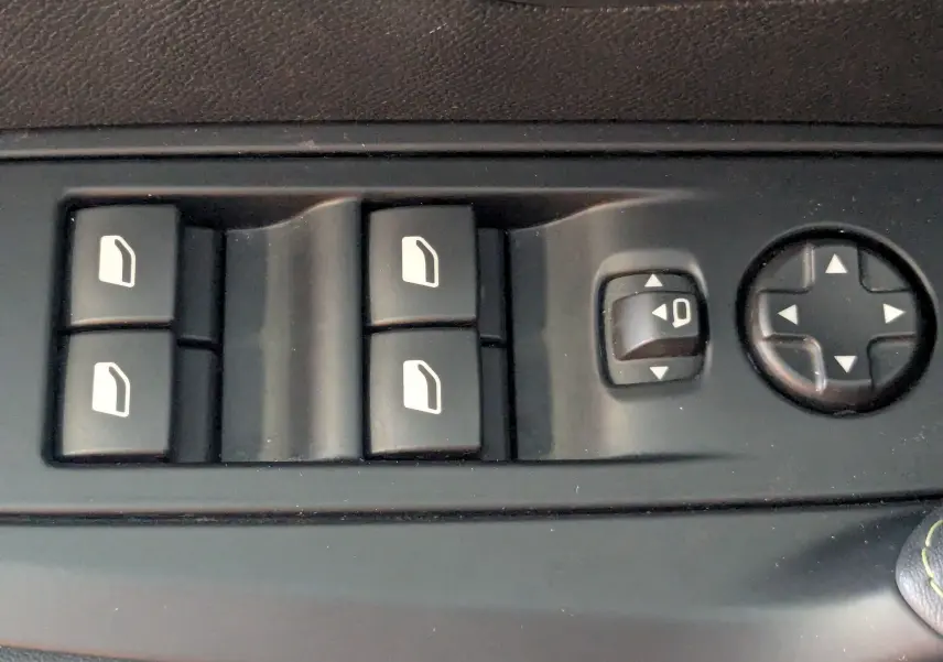Gros plan sur les commandes de lève-vitres et réglage des rétroviseurs côté conducteur d’une Peugeot 208 gris Selenium.