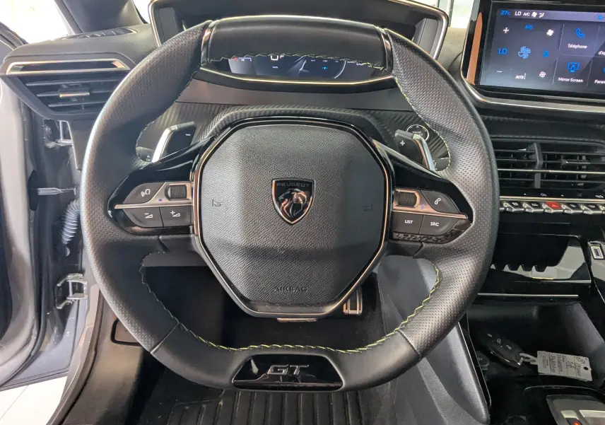 Vue rapprochée du volant cuir noir avec surpiqûres vertes et badge GT du Peugeot 208 Hybrid 145 e-DCS6 GT.